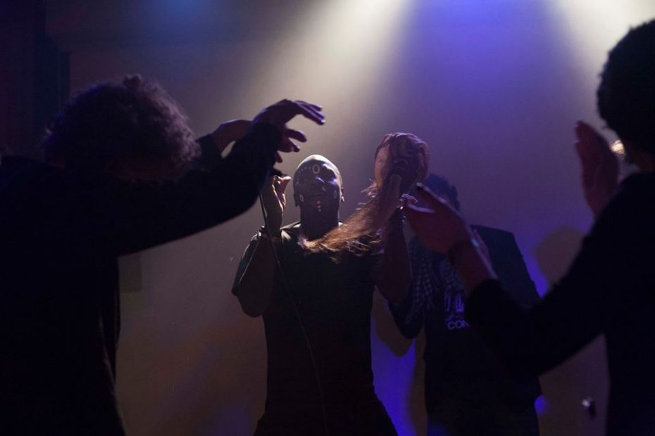 Silhouette of four figures dancing and arms raised, with a Black man central. They are set against a blue and cream -lit background. Image commemorating WORM's Afrofuturism Now! Festival November 2015.