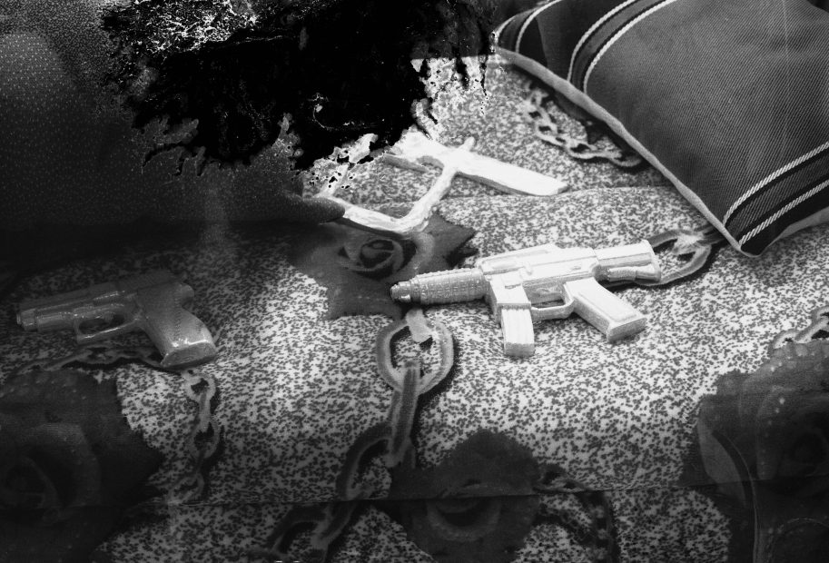 Black and white photograph taken from above of a patterned, maybe carpeted or quilted surface with cushions and plastic guns; a pistol and an automatic rifle. Used in a WORM interview with the artist Susanne Khalil Yussef 2019.