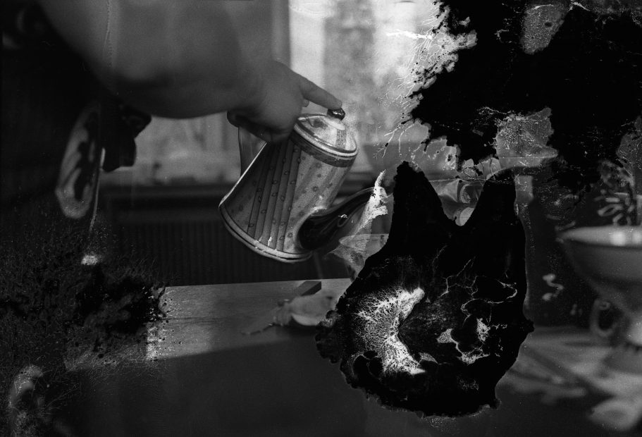 A treated black and white photograph, maybe deliberately treated to suggest a damaged print of a hand holding a coffee pot in the act of being poured, with a finger held on the lid. Used in a WORM interview with the artist Susanne Khalil Yussef 2019.