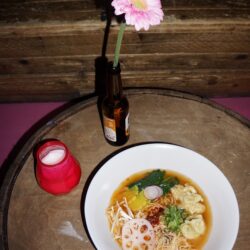Colour photographs of vegan dishes available at Wunderbar in WORM. A bowl of saoto soup on a table, next to a flower in a bottle.
