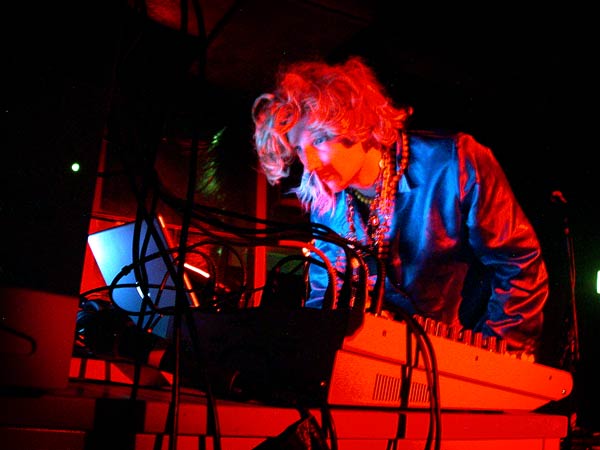 Colour photo of a man wearing a wig peering at a laptop onstage. Part of the WORM tribute to Wim T. Schippers.