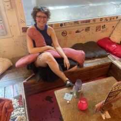 Colour photo of Dari Zaeva from Pirate Stitching Club, sitting in WORM's Stube, with a pink worm wrapped around her 2026