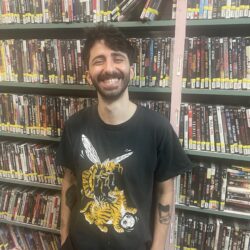 Colour photo of Riccardo Calandro grinning in front of the wall of DVDs