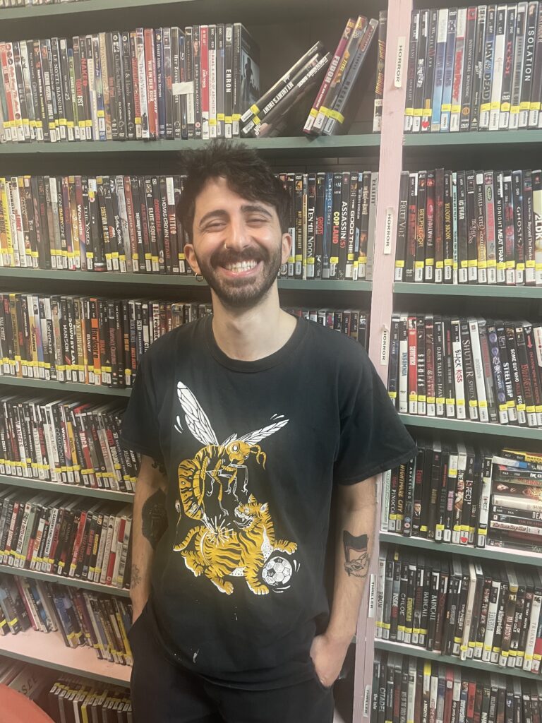 Colour photo of Riccardo Calandro grinning in front of the wall of DVDs